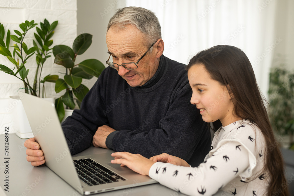 Fototapeta premium Portrait of grandfather and granddaughter doing homework with laptop.