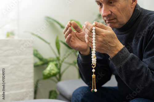 Praying hands of an old man holding rosary beads.