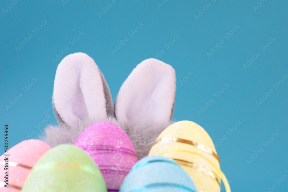Background with easter hidden furry grey white little soft rabbit long ears and multi colored eggs in green, pink, yellow with copy space in blue backdrop
