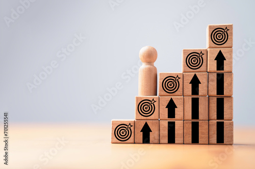 Wooden miniature figure standing on second step of staircase with dartboard and up arrow for continuous enhancement business objective target and goal concept. photo