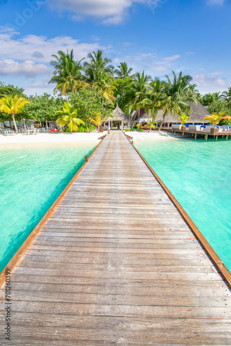 Luxury travel landscape. Water villas  wooden pier bridge leads to palm trees over white sandy shore close to blue sea  seascape. Summer panoramic vacation  beach resort on tropical island paradise 