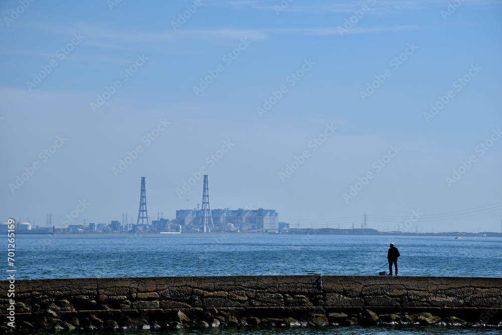 火力発電所の対岸で釣りをする人。