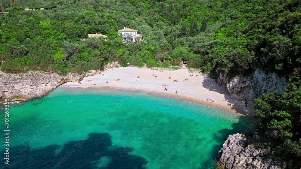 Aerial view of Rovinia Beach with tourists enjoying vacation with dreamy crystal-clear turquoise waters. View of mesmerizing white-pebble shore mixed with sand and green forest in the background.