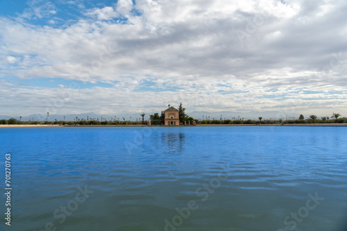 Photo of the Menara Gardens in the city of Marrakech. Photo of the lake with the house at the end of the lake. The house reflected in the lake. Cloudy day.