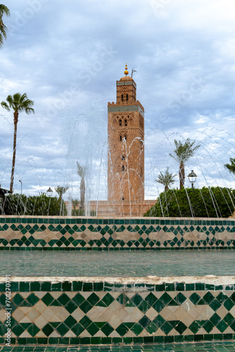 Photo of the tower of the Koutoubia mosque. Park with a fountain. Cloudy day.