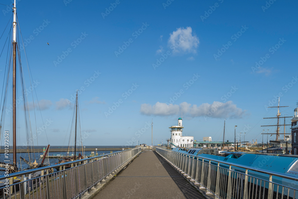 View on the Hoge Willemskade, walkway of the Nieuwe Willemshaven, in Waddensea harborcity Harlingen, Friesland, the Netherlands, with view to the harbor control tower , train and sailingboats