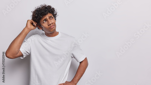 Quadro em tela Confused Hindu man scratches head and looks aside feels doubtful wears casual t