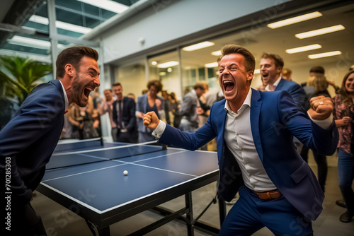 Two enthusiastic men in business suits celebrate during a competitive game of table tennis in a lively office environment, showcasing teamwork and office recreation photo