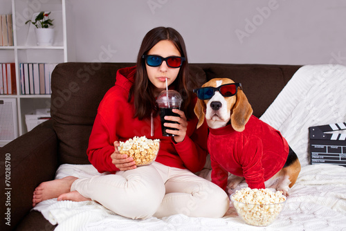 A young girl with her dog beagle in 3 d glasses is sitting on the couch and watching a movie at home.  photo