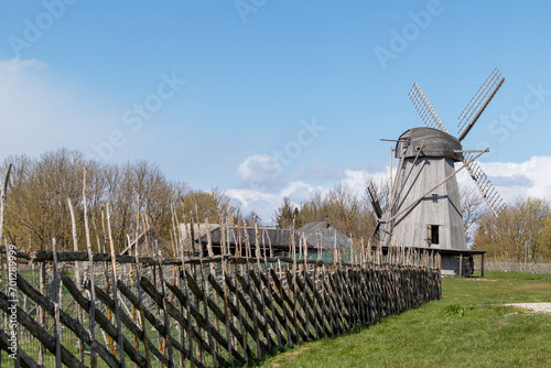Wooden windmill with a wooden fence on a background of grass and blue sky