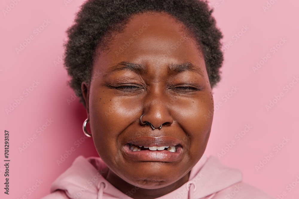 Close up portrait of dark skinned woman with curly hair has upset doleful expression cries from despair expresses negative emotions being offended has problems isolated over pink background. Close up portrait of dark skinned woman with curly hair has upset doleful expression cries from despair expresses negative emotions being offended has problems isolated over pink background.