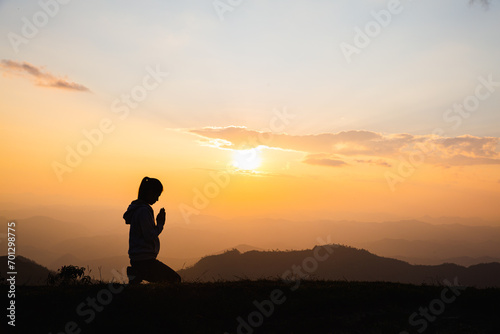  Silhouette of Woman praying for thank god praying with her hands together to think of a loving God, we praise God with light flare in the green nature.
