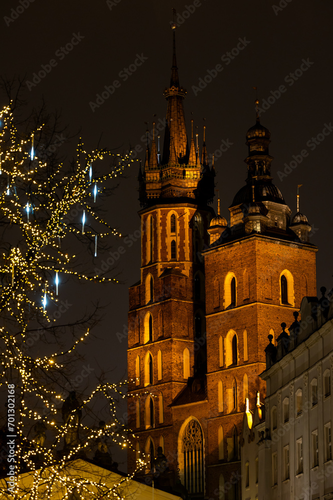 Fototapeta premium The tower of St. Mary's Basilica in Krakow against the background of Christmas decorated trees. Night view of Krakow's Old Town.