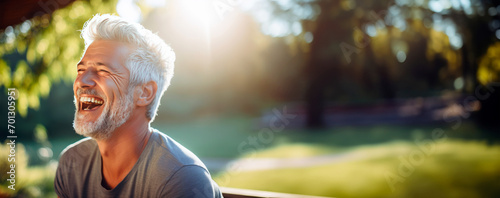 Senior trim man in gray t-shirt with neatly coiffed silver hair laughing and happy in background of summer green outdoor garden. The health of elderly. Joyful moments. Golden years. Banner. Copy space