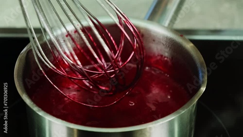 Chef uses kitchen tools to stir blend of beetroot juice and reagent in saucepan. Mixture simmers evaporating any excess moisture