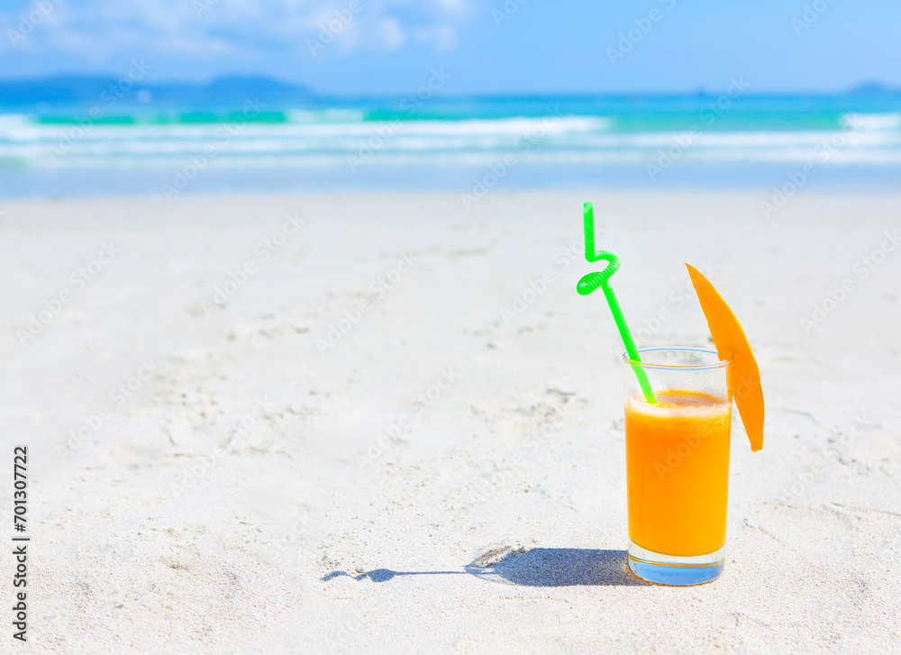 Glass of orange colour juice and sand and sea