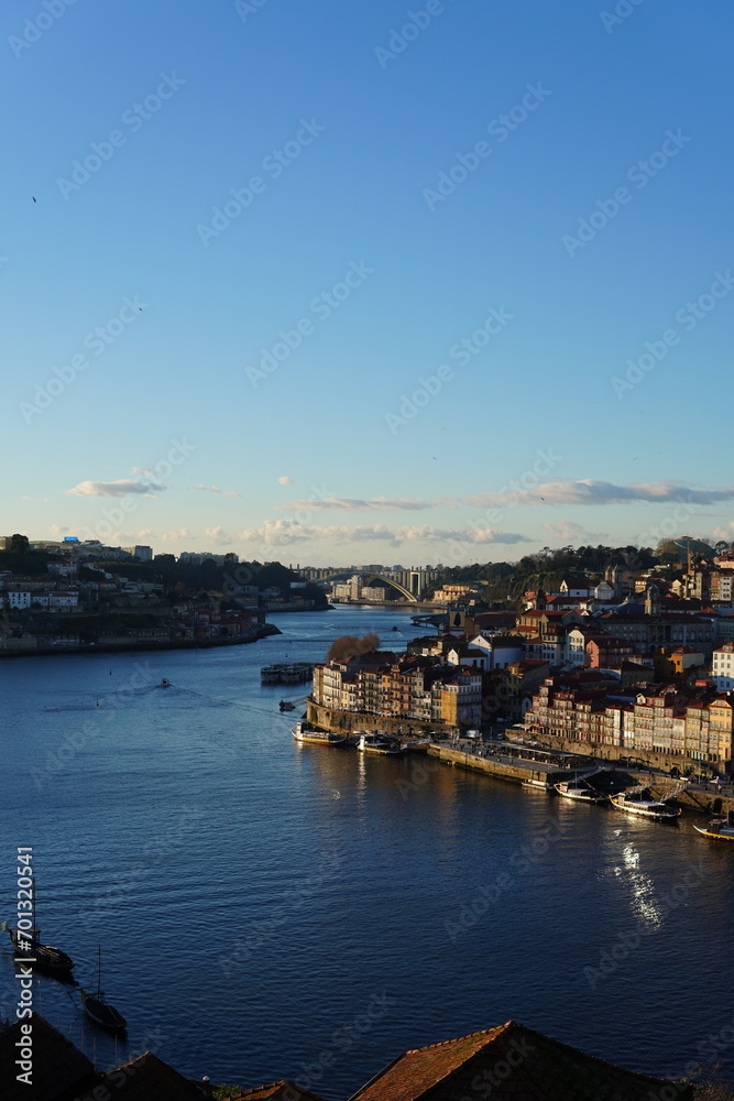 This image shows a row of cozy riverside homes in the Ribeira district of Porto, Portugal. The homes are built of stone and wood and have red-tiled roofs. They are located along the banks of the Douro