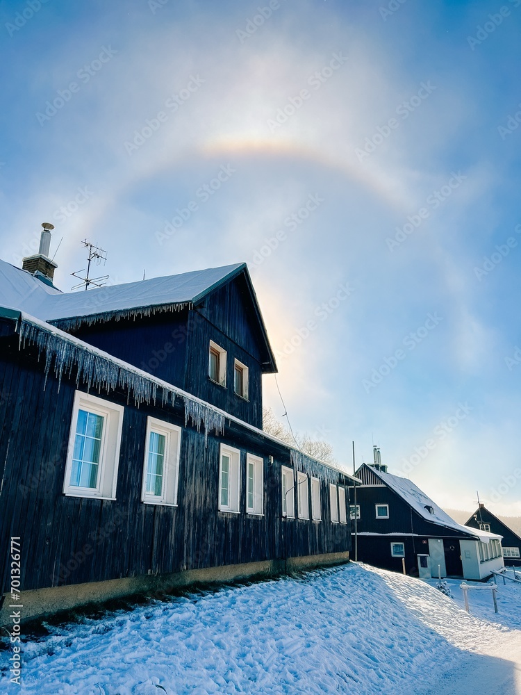 Halo effect in snowy mountains, village with houses, frosty day