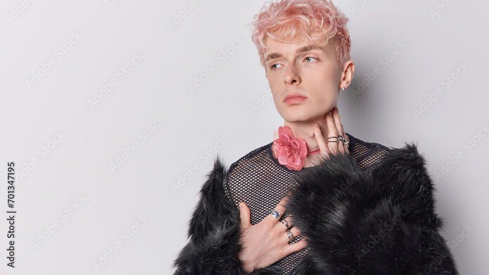 Stylish pink haired adult man wears black fur coat and flower chain around neck concentrated aside being deep in thoughts isolated over white background copy space for your promotional content Stylish pink haired adult man wears black fur coat and flower chain around neck concentrated aside being deep in thoughts isolated over white background copy space for your promotional content