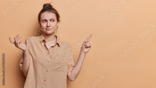 People positive emotions concept. Studio shot of young beautiful happy European girl standing on left isolated on beige background looking and pointing at blank space for your promotion wearing blouse