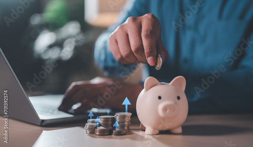 investment, money, coin, finance, financial, save, wealth, budget, cash, currency. a man put on casual shirt of hand putting a coin in the piggy bank, pile of coins on the table for retire plan.