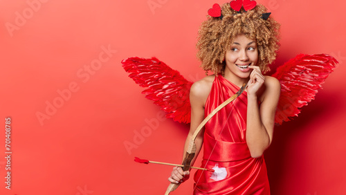 Happy St. Valentines Day. Studio shot of young pretty cheerful smiling African american girl standing on right in cupid costume looking at blank space for promotion thinking about something pleasant © Wayhome Studio