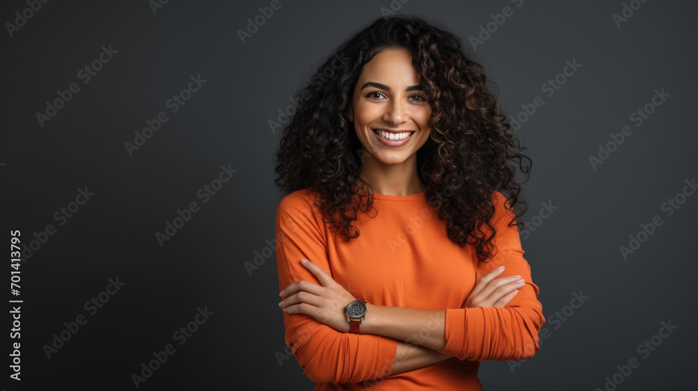 Confident woman with curly hair, smiling at the camera, wearing a bright orange shirt, with her arms crossed. Confident woman with curly hair, smiling at the camera, wearing a bright orange shirt, with her arms crossed.