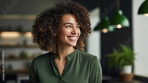 Woman with curly hair and a confident smile, standing with her arms crossed in an office environment.