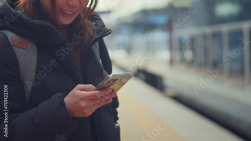 Closeup - Happy woman using smart phone while waiting on station platform, Female using mobile phone at train station, Enjoying travel concept