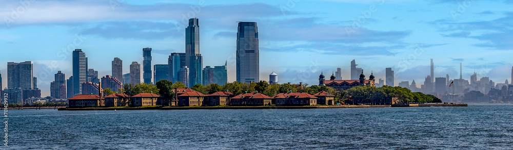 Photograph of Ellis Island, from Liberty Island where the iconic statue of New York (USA) is located and the Big Apple skyline in the background. - obrazy, fototapety, plakaty 