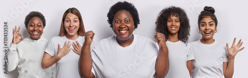Five diverse young women react to something awesome clench fists have happy faces make okay gesture reassures everything is okay feel glad wear casual t shirts isolated over white background. photo