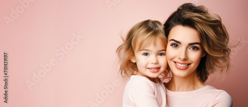 Portrait of a beautiful young woman and her little girl in a pink hoodie on a pink background