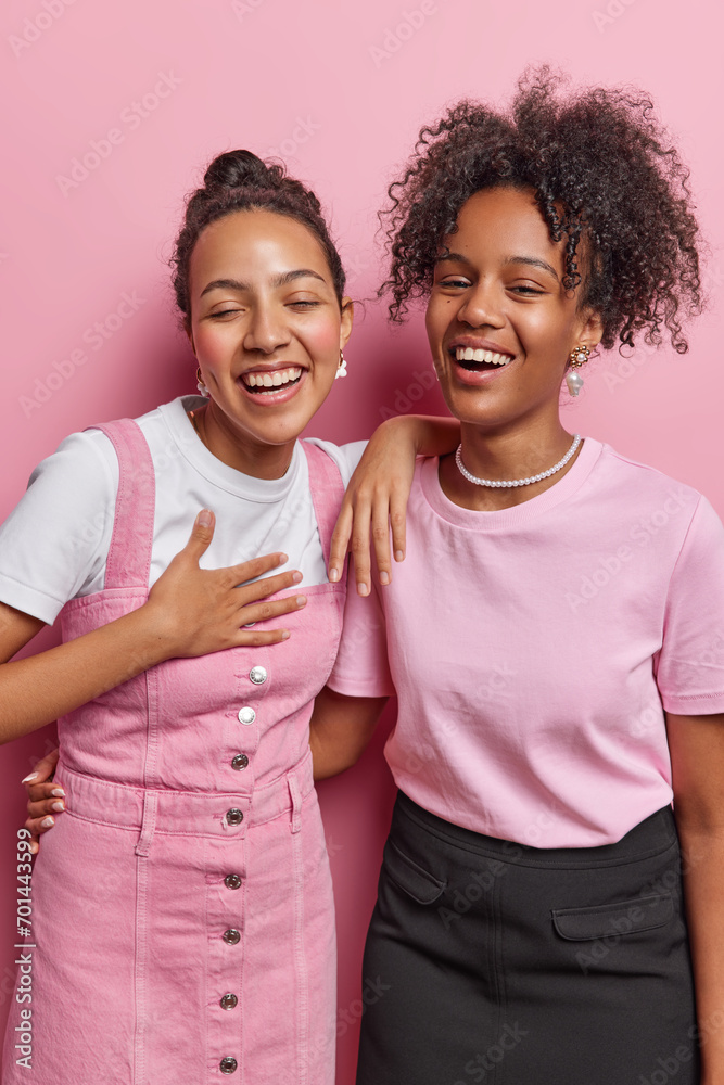 Vertical shot of overjoyed women cannot stop laughing at something funny express sincere emotions dressed in fashionable clothes isolated over pink background. People friendship and happiness concept Vertical shot of overjoyed women cannot stop laughing at something funny express sincere emotions dressed in fashionable clothes isolated over pink background. People friendship and happiness concept