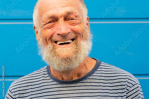 75 year old senior man laughs while having a good time outdoors. Portrait with blue background. Leisure and people concept