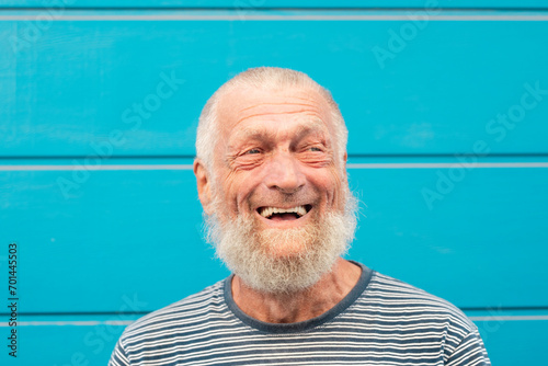 75 year old senior man laughs while having a good time outdoors. Portrait with blue background. Leisure and people concept photo