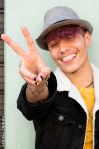 Success and victory hands finger sing for young man boy teenager hispanic race and violet hair and hat - happy people satisfacted - trendy black color nails - joyful teenager outdoor photo