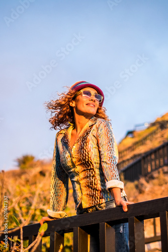 Beautiful woman standing and ejoying the sunset sun light on the face - portrait of young pretty female people in outdoor relax leisure activity - tourist look and trendy clothes modern style © simona