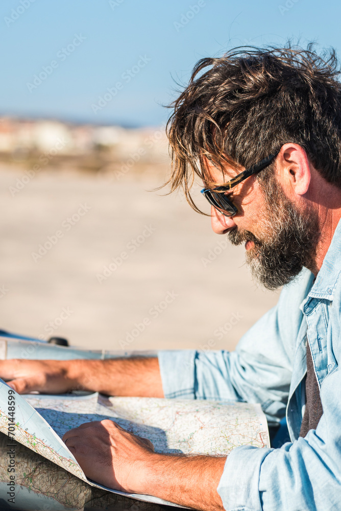 Man look a paper road trip map standing outside the car with blue sky and ground desert in background - concept of travel and adventure lifestyle people - outdoor leisure travel vacation activity