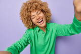 Overjoyed curly haired woman dressed in casual green jumper opening arms for embrace smiles broadly feels very happy poses against purple background. Cheerful female model gives hug to someone