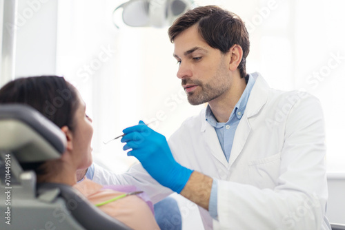 Professional male dentist doctor making regular check up for female patient in modern dental clinic