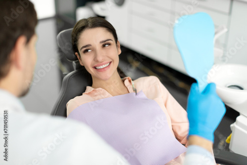 Female patient after dental treatment in clinic talking with doctor, woman sitting in chair in stomatological cabinet and enjoying her beautiful smile photo