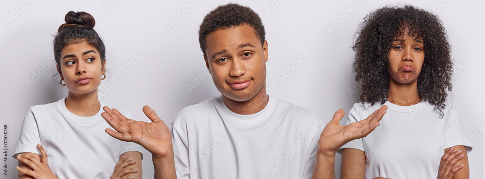 Φωτογραφία Studio shot of African man spreads palms feels hesitant stands between two pensive women cannot make decision dressed in casual t shirts isolated over white background