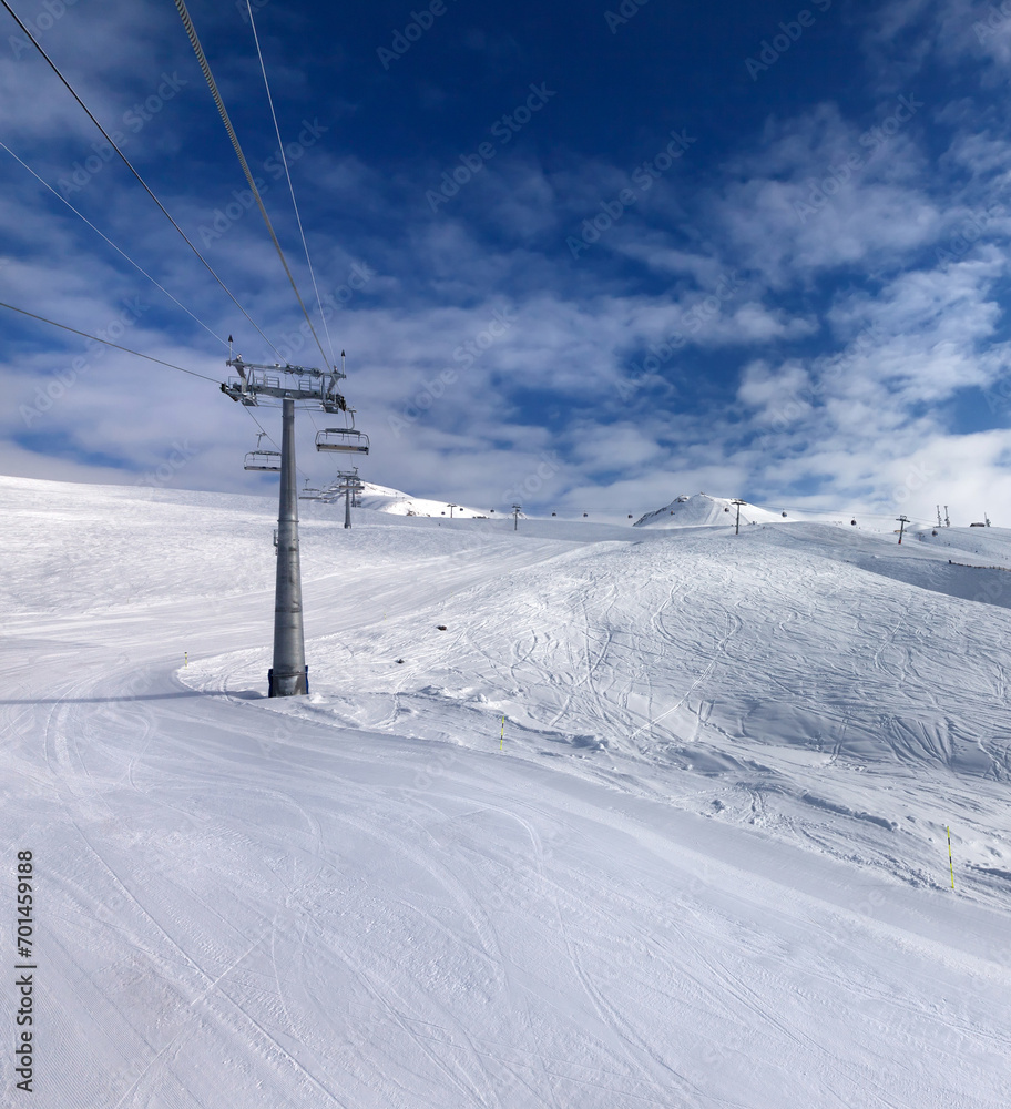 Ski slope, chair-lift on ski resort and blue sky with sunlight clouds