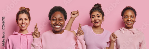 Four positive women smile gladfully dance carefree have good mood keep fingers crossed believes in good fortune dressed casually isolated over pink background. Peope and happy feelings concept photo