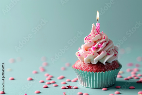 Cupcake with red sprinkles and lit candle on a blue background.
