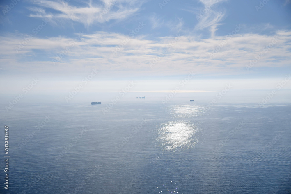 A shot of the Mediterranean Sea, from Alicante, Spain, with blue sky and clouds, hazy atmosphere, sun reflection and tiny ships close to the horizon. 