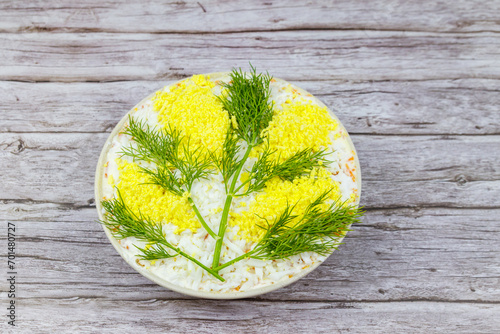 Traditional russian layered salad Mimosa decorated with sprigs of mimosa (made of eggs yolk and dill) on wooden table. Top view