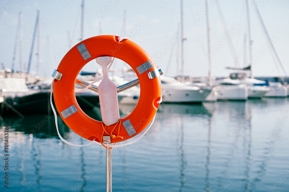 Red lifebuoy on a metal stand with white plastic fastener by the sea