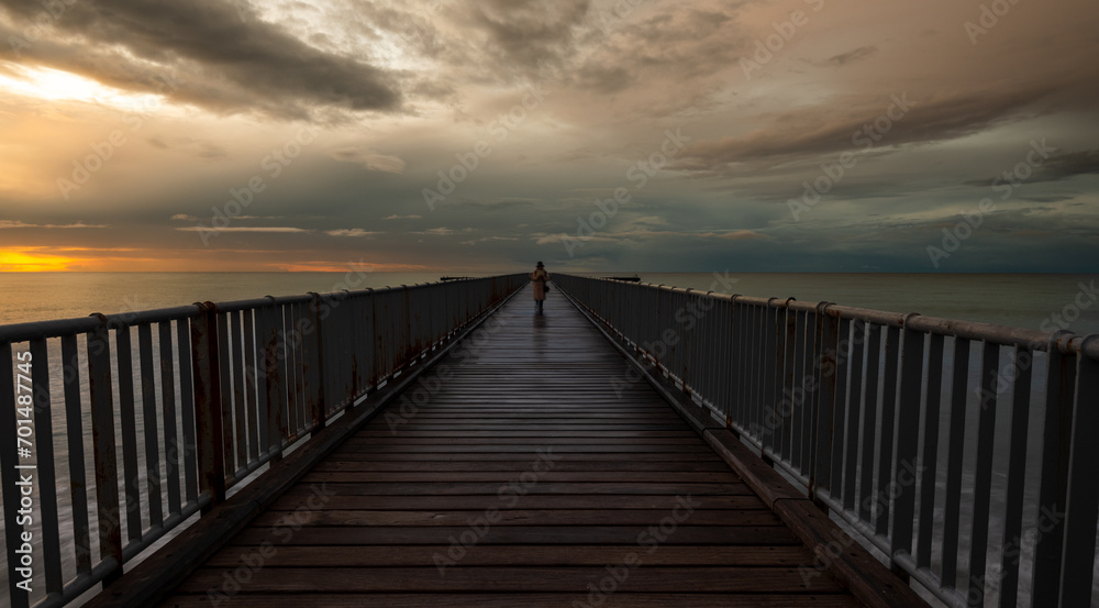 Person walking alone on a pier enjoying dramatic sunset at the sea. Exploring nature