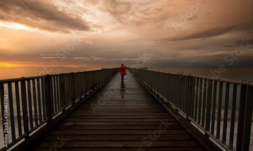 Person walking alone on a pier enjoying dramatic sunset at the sea. Exploring nature © Michalis Palis